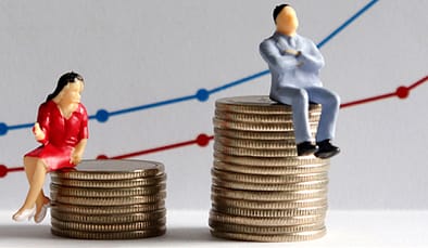 The concept of gender pay gap. A miniature man and a miniature woman sitting on top of a pile of coins at different heights in front of a bar graph.